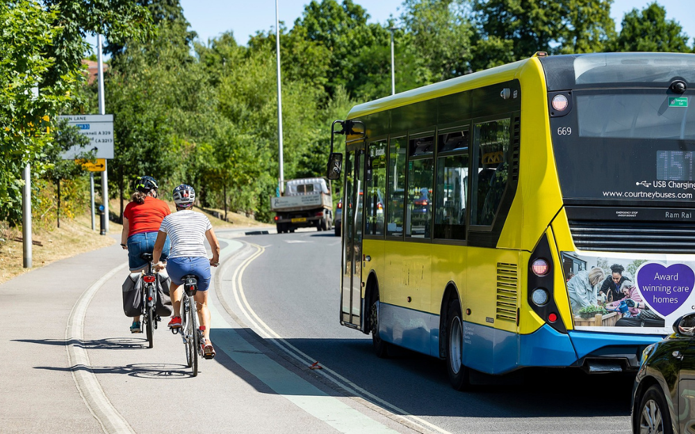 two cyclists riding side by side along a segregated cycle track, with a bus passing them on the road beside it