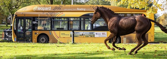 the leopard 3 bus driving through Arborfield Green in autumn, with a statue of a running horse in the foreground and facing the same way