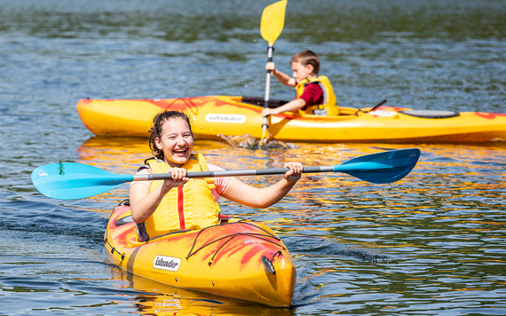 Two people wearing life jackets kayak on a lake.