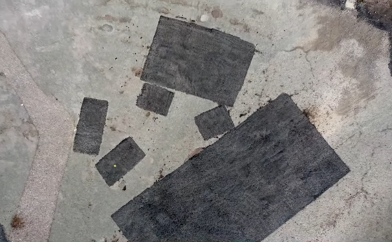 aerial view of a road where several squares have been cut out and filled in with fresh asphalt as pre-patching