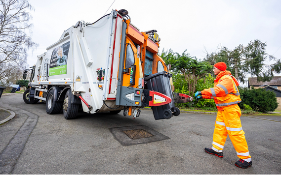 A member of the waste and recycling collection team in high visible overalls is behind a white bin lorry