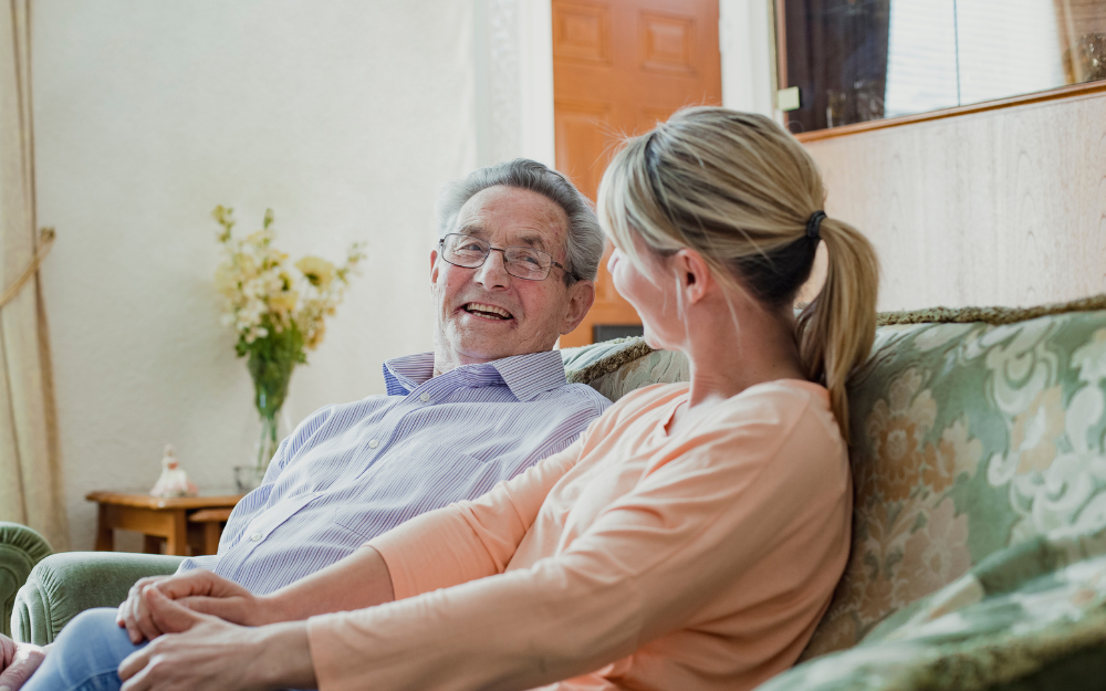 Two people sitting on a sofa, engaged in conversation inside a cozy room.