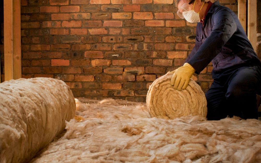 a man in a face mask unrolls a thick roll of insulation inside somebody's loft