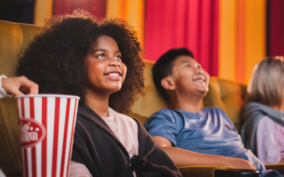 Two children in the cinema, smiling and eating popcorn