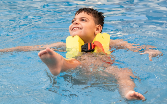 A child smiling and floating on their back in a swimming pool