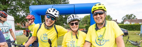three adults in bike helmets and matching yellow tops smiling at the finish line of a bike ride