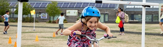 a little girl in a bicycle helmet smiling as she ducks and rides under a bar on an obstacle course