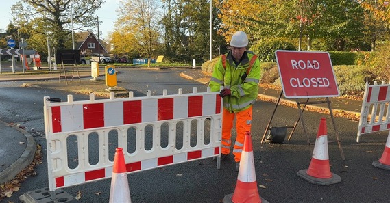 a man in hard hat and high vis moves a plastic barrier to close a road