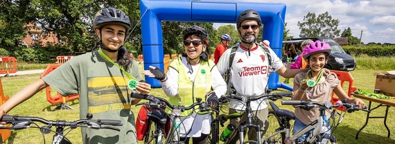 a family of four, with two older children, pose on bikes and smile at the finish line of a riding event