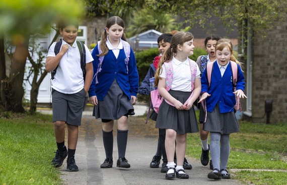 four primary-aged girls in school uniform walk through a park and chat