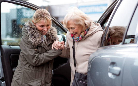 A volunteer helping an older lady out of the car