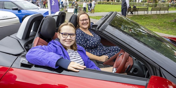 two young women sit in the front seats of a red open-top electric vehicle and smile at the camera