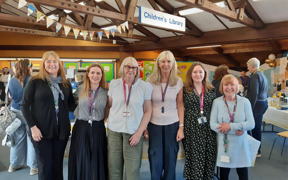 Woodley Library Staff, six staff facing the camera with customers in the background.  Some gold and white birthday balloons