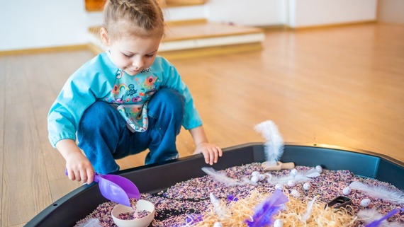 a child crouches by a sensory play tough tray on the floor