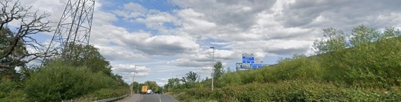 driver's eye view of a road running alongside the M4 motorway, with a pylon on land to the left