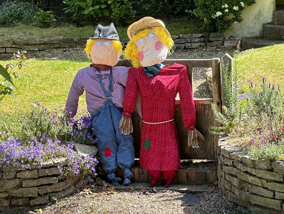 a male and female scarecrow posed at the entrance to someone's front garden with arms around each other