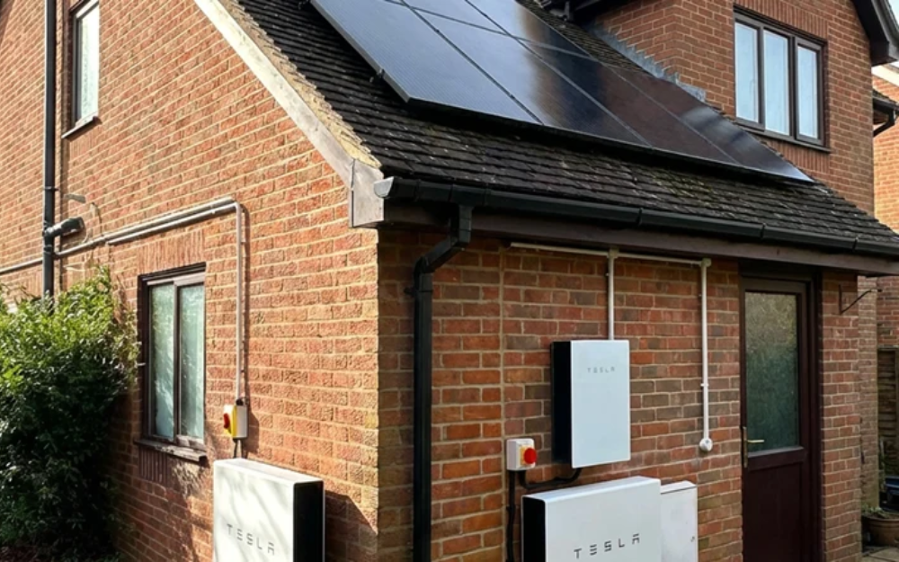 Wall-mounted home battery system installed outside a brick house, part of a solar energy setup