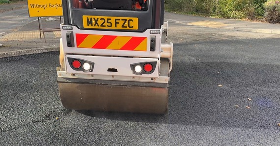 close up on the front wheel of a roller pressing down a fresh laid asphalt surface