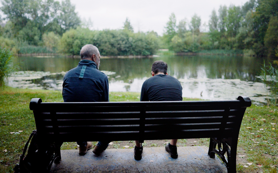 A man and a boy sat on a bench by a pond