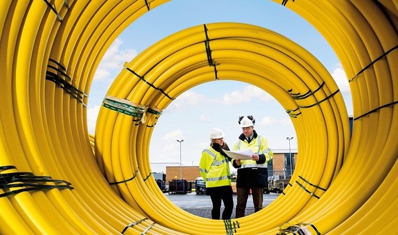 view down the centre of a huge coil of yellow plastic pipes, with two engineers in high vis checking notes at the end of it