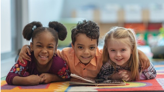 three children lying on the library floor reading a book together