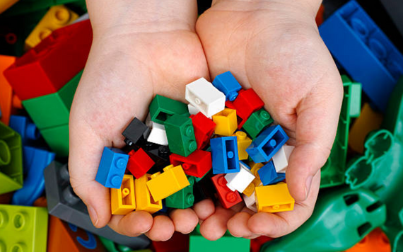 Lego Club - child's hands are holding multi-coloured lego bricks with a back groups of jumbled lego bricks