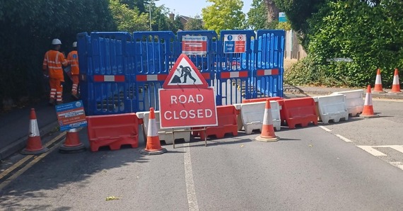A road closed off by blue plastic barriers and people from Thames Water walking alongside it