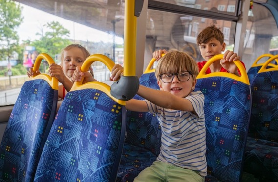 a group of four children aged about seven, sitting on the back seats of a bus and smiling