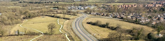 aerial view of a road in the borough with a green space to the left and housing in the distance