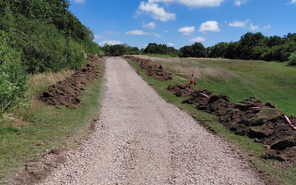 New footpath under construction across open grassland at Ashenbury Park, with excavated soil alongside the route.