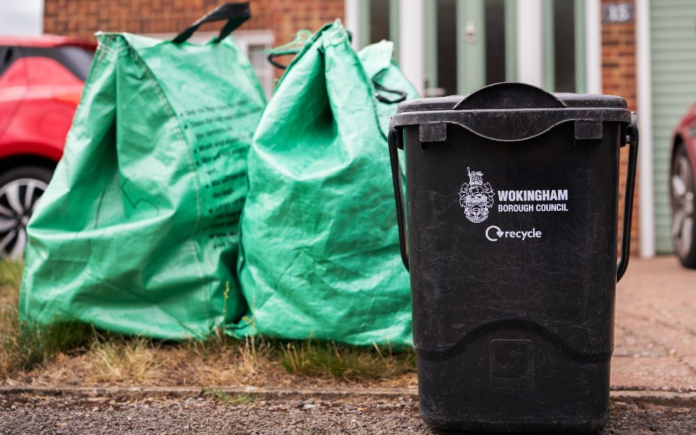 Black food waste recycling bin and green recycling bags placed at the kerbside outside a home, ready for collection.