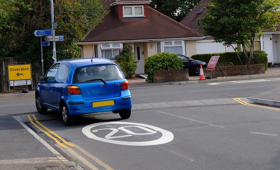 a car emerges from a side road on to a main road, crossing over a raised cycleway over the mouth of the junction