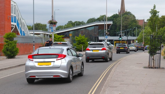 a line of cars driving up Station Approach in Wokingham, past the station, with the multi-storey car park in the background