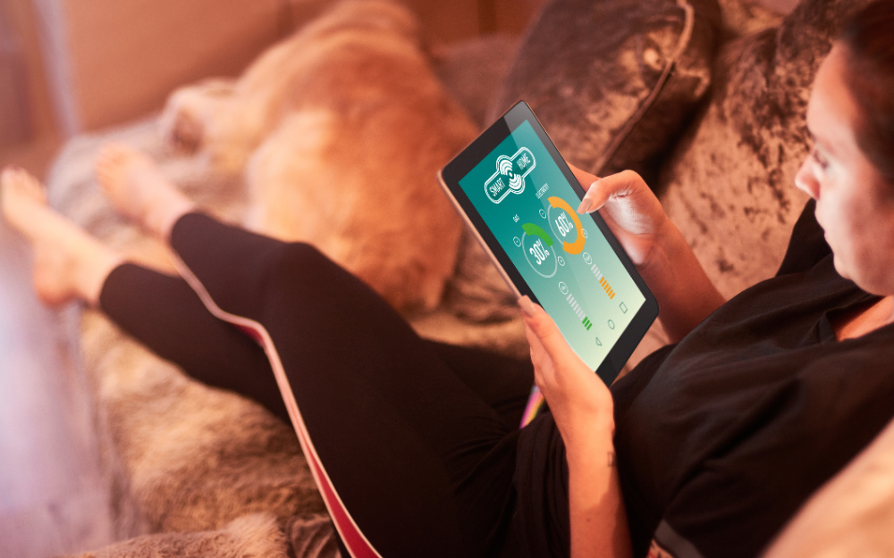 A person lying on a sofa, looking at energy usage infographics on a tablet device.