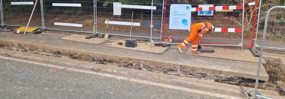 a Thames Water worker in high vis sweep debris away from a trench in the road