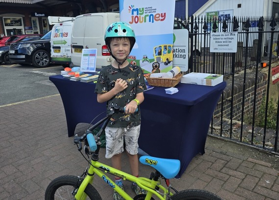 a young boy with a bicycle, wearing a helmet, stands in front of a My Journey stall at Twyford station