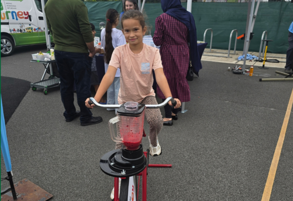 a young girl rides an exercise bike connected to a smoothie maker filled with red fruit