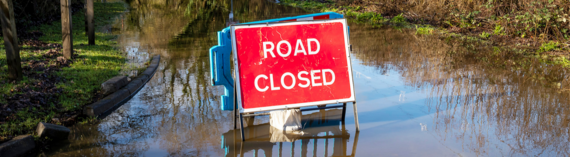 A road closed sign in the middle of a flooded road in a rural location