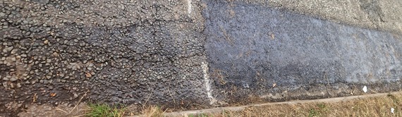 a section of newly patched road, with an unrepaired section next to it with a crack running along the carriageway