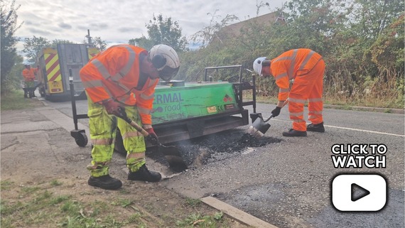 two men breaking up a road with spades, with a play button and the words "click to watch"