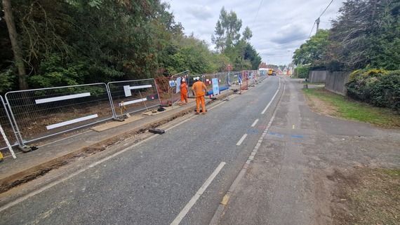 very wide shot of a trench running along the length of Barkham Road, with Thames Water workers erecting a mesh fence alongside it