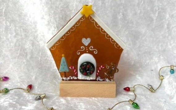 A fused glass ginger bread house standing up with some lights 