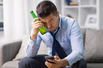 Man staring sadly at his phone with beer in his hand