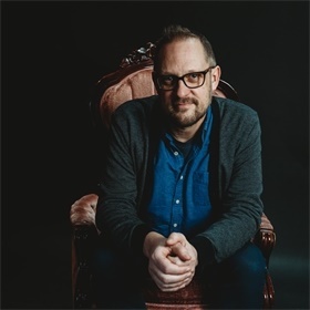 Photograph of author Peter Swanson sitting in a chair. Photograph credit: Emily Tirella.