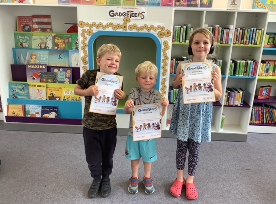 Three children holding certificates in the library