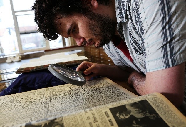 Man looking at archival documents with a magnifying glass