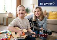 A child with Downs syndrome playing the guitar with a white adult woman, also playing the guitar, against the background of a living room