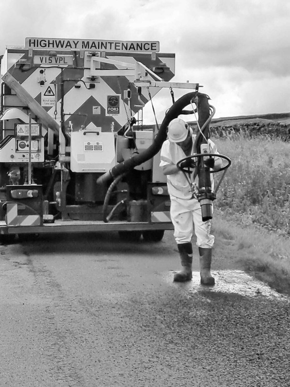 A highway maintenance jet patcher vehicle and worker performing a road repair