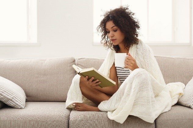 A lady sat on a sofa with a book and a mug