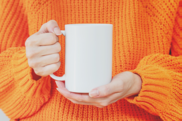 White mug being held by a woman wearing an orange jumper